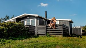 Sort sommerhus med glade børn og blå himmel