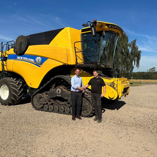 To mænd giver hånd foran en stor New Holland maskine på en mark