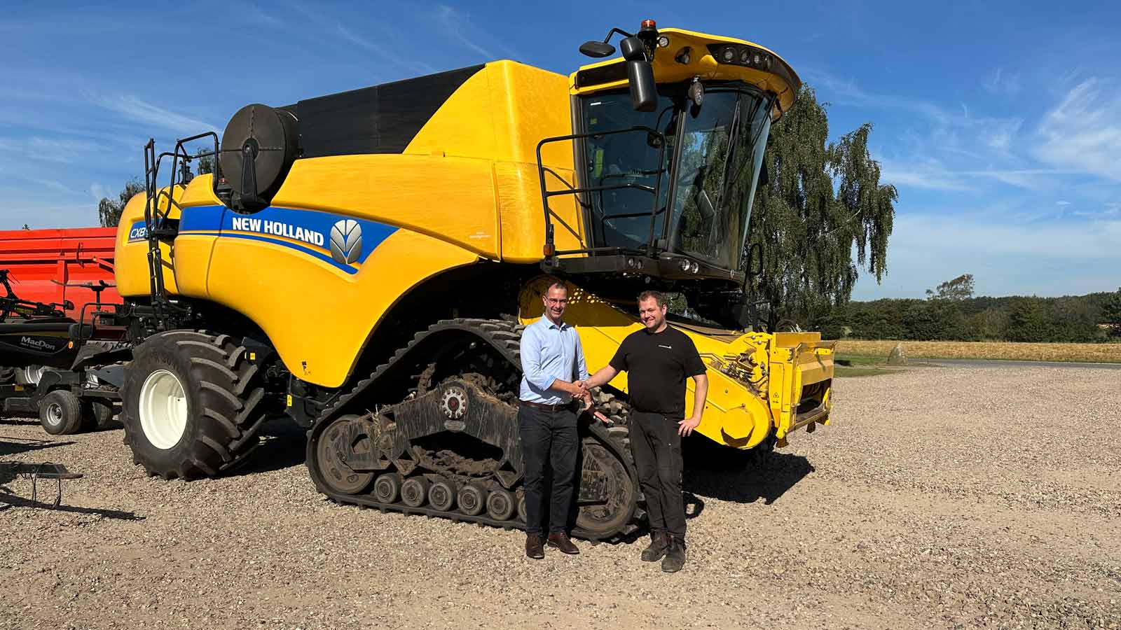 To mænd giver hånd foran en stor New Holland maskine på en mark