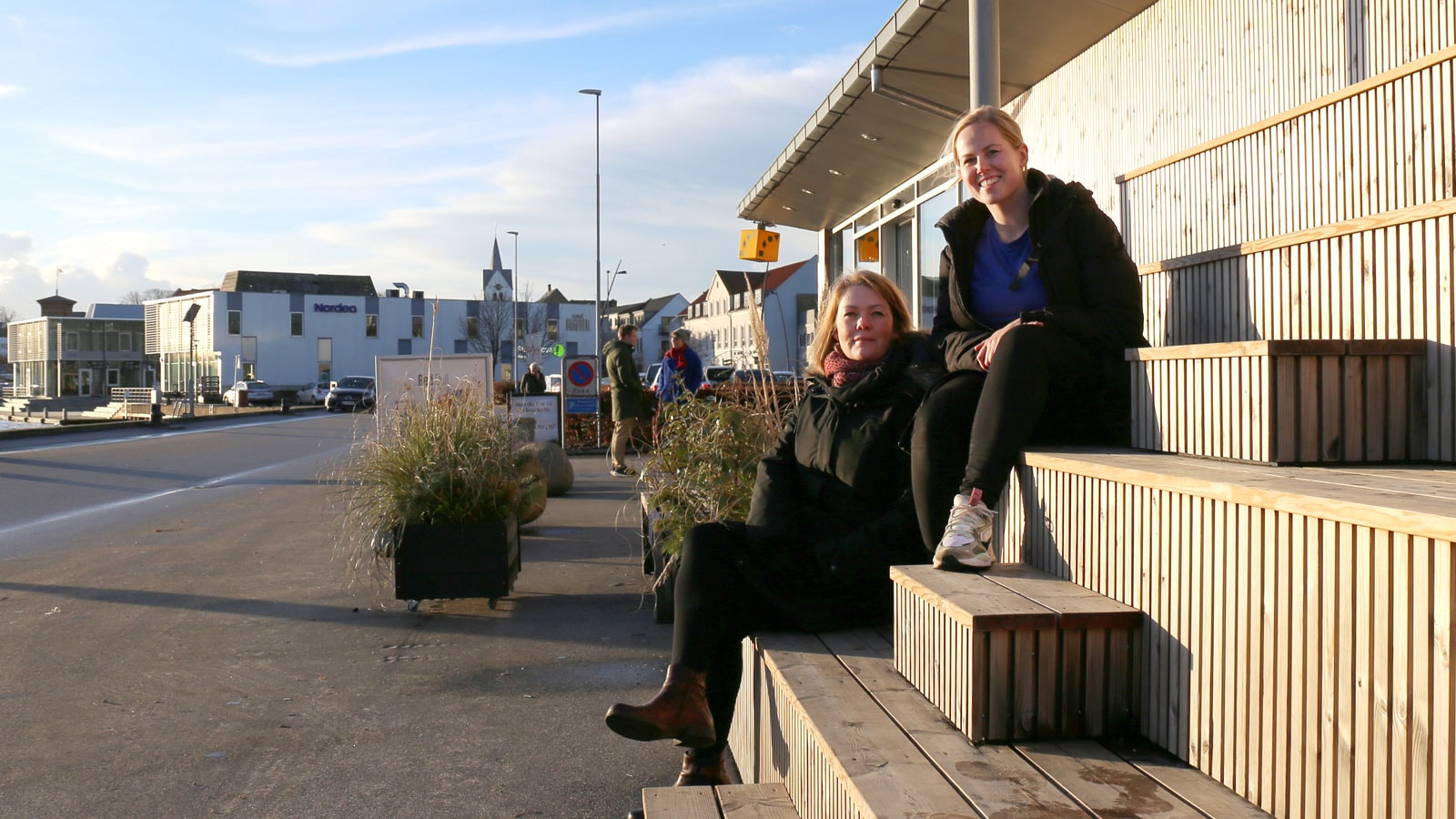 To kvinder på en bænk foran en el-tankstation.