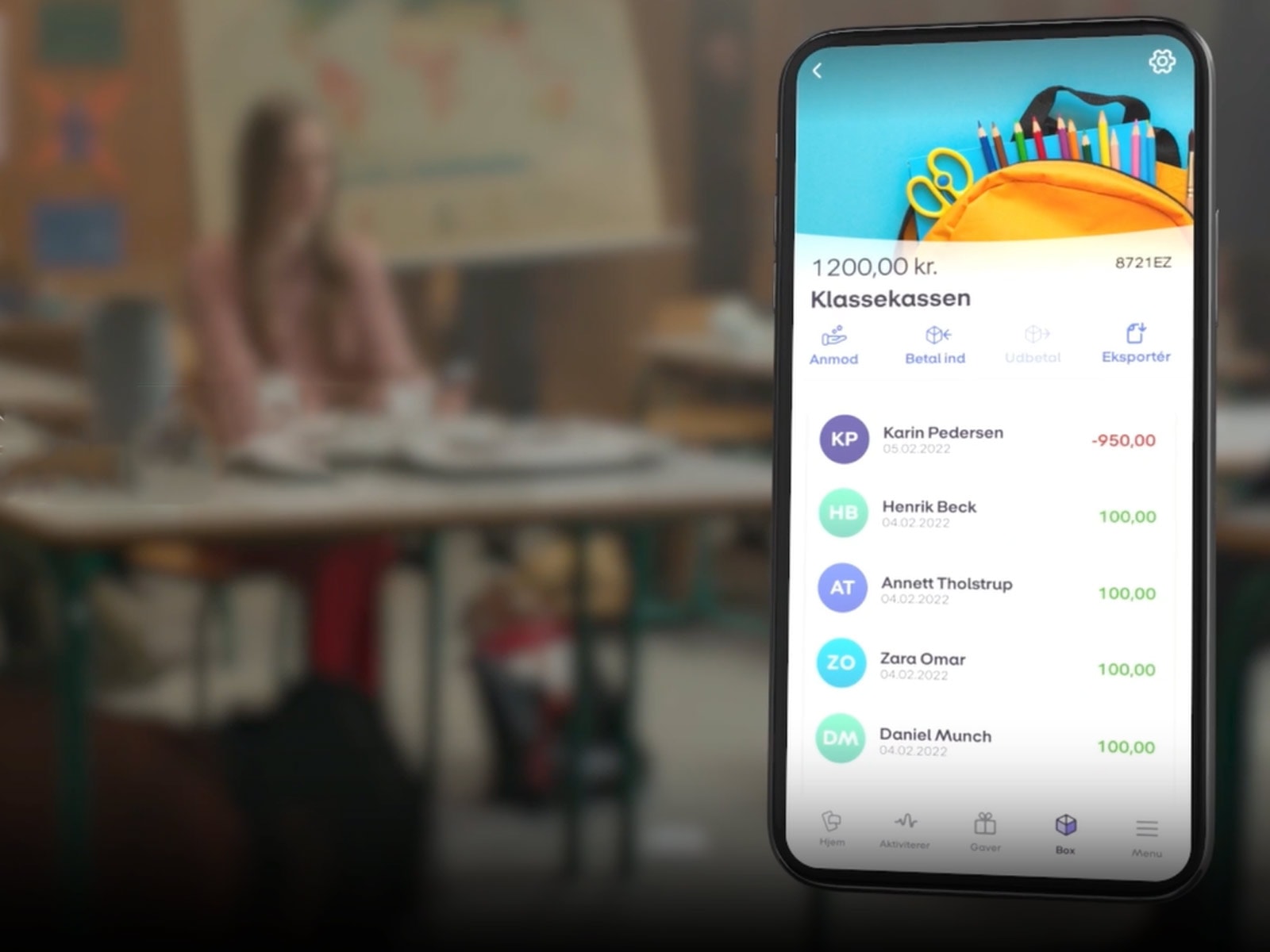 Mobiltelefon med skærmbillede fra Mobilepay Box og et klasselokale i baggrunden