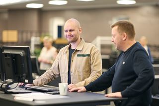 To mænd står og arbejder foran en computer
