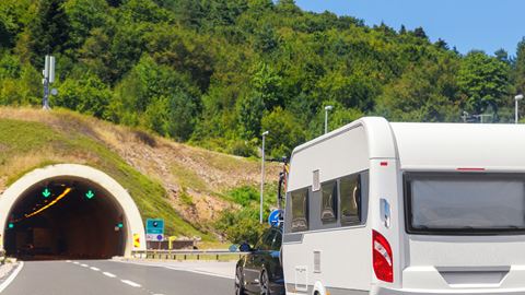 Bil med campingvogn på vej ind i en bjergtunnel