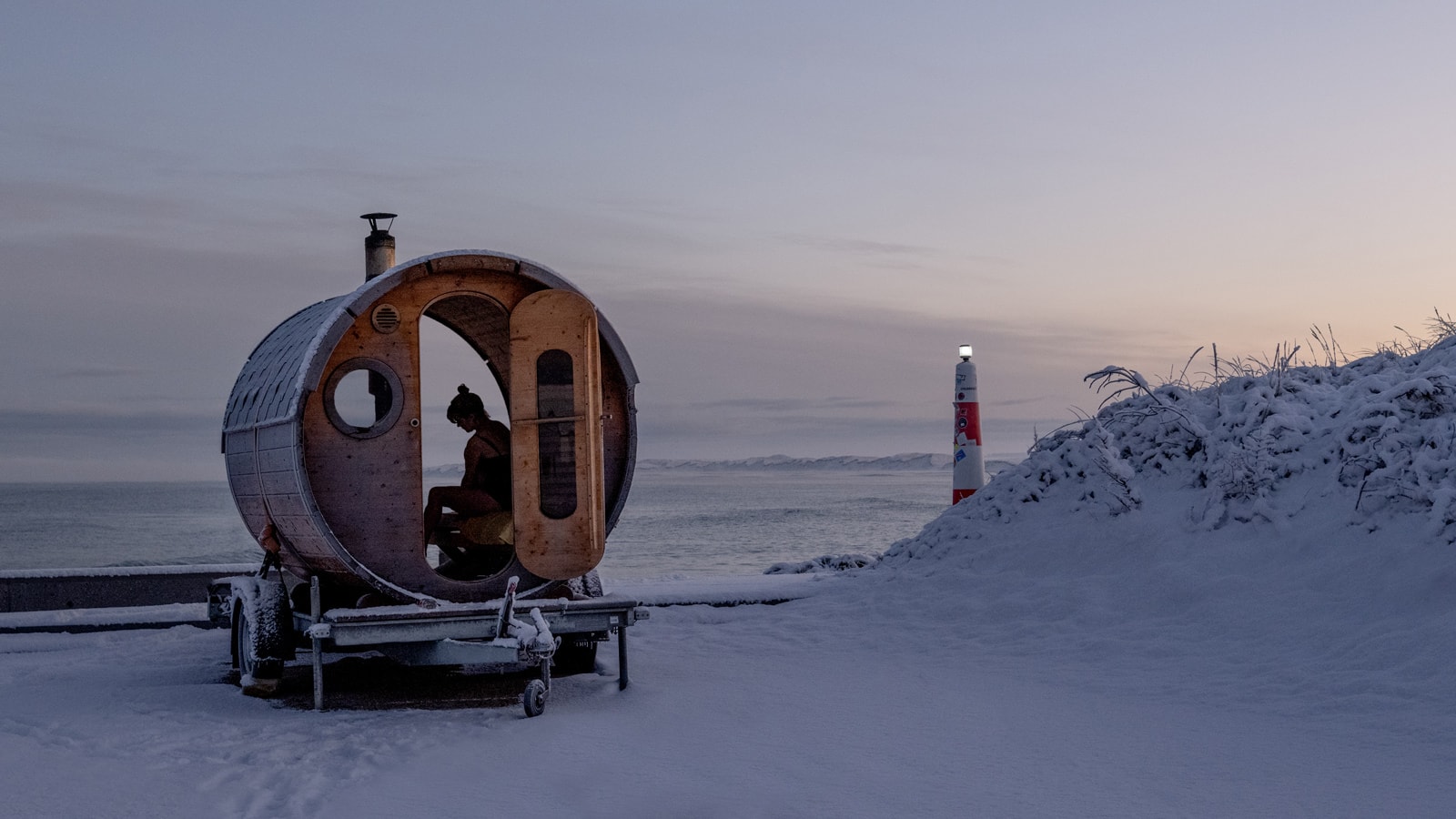 Snedækket strand med tøndesauna og en kvinde indeni