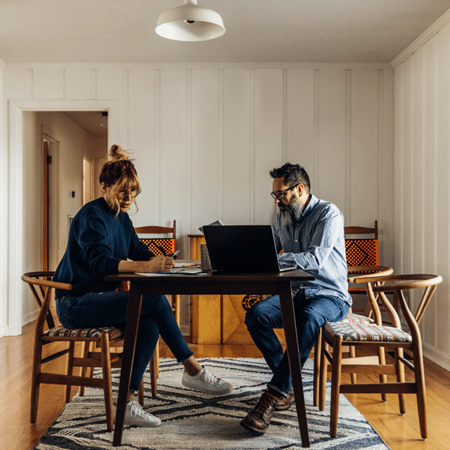 To personer ved et bord med computer og skriveredskaber