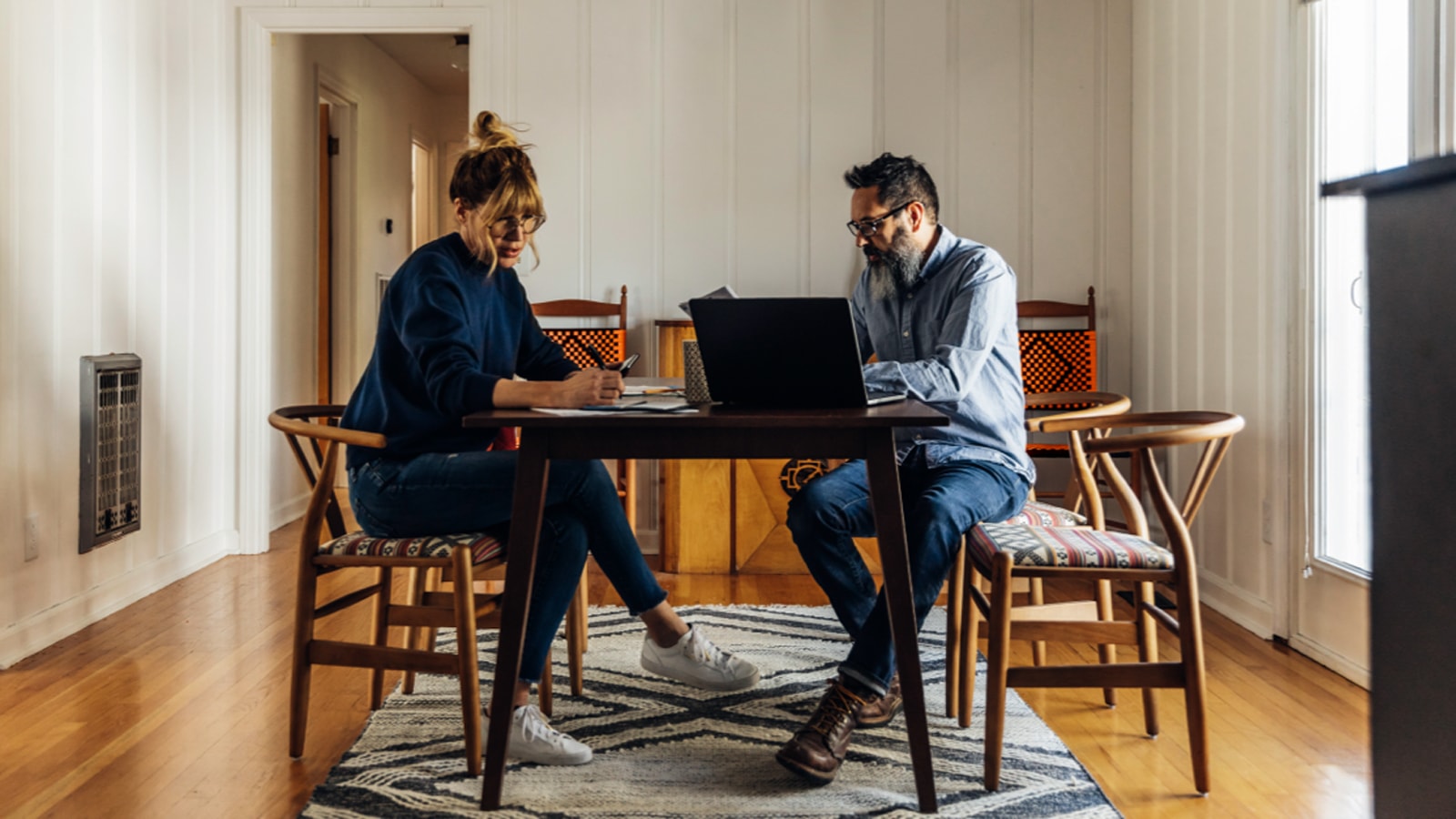 Do personer ved et bord med coputer og skriveredskaber